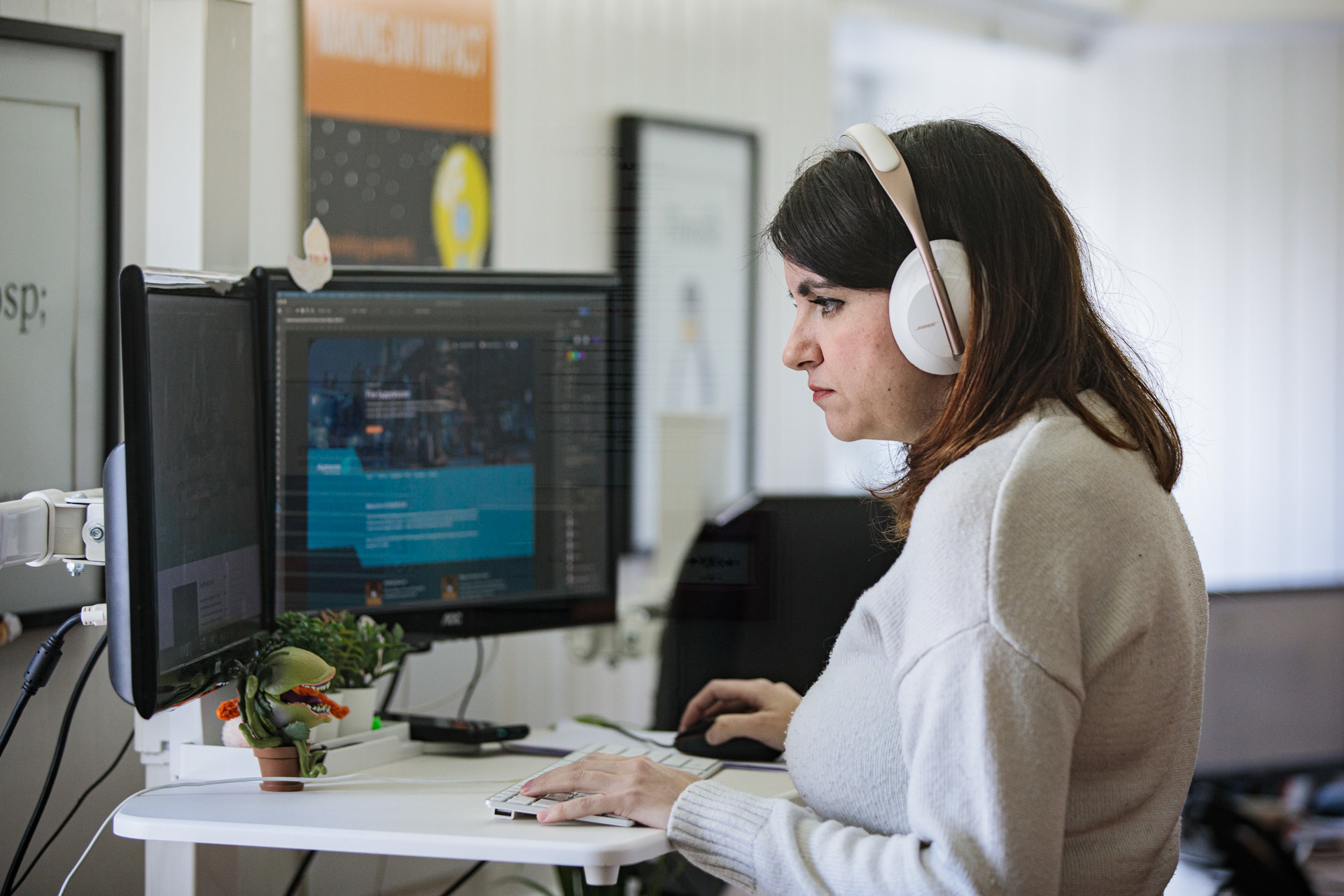 A woman wearing headphones, looking at her desktop computer